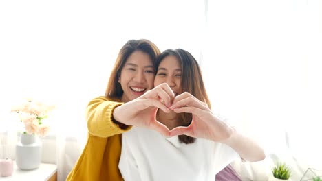 young asian lesbian lgbt couple forming heart shape with hands on bedroom at home.