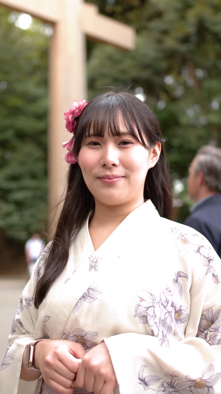 Eine japanische Frau in einem floralen Yukata lächelt vor einem Shinto-Torii-Tor.
