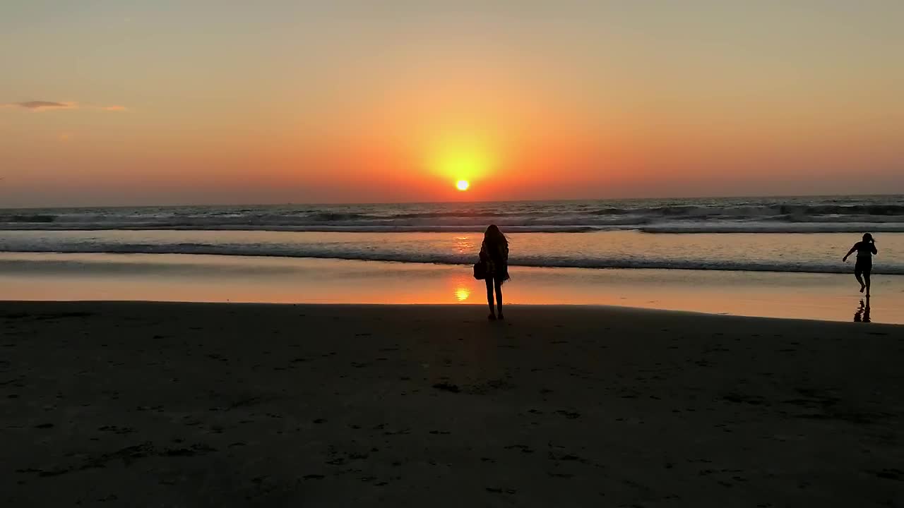 Silhouette di una giovane donna in piedi da sola sulla spiaggia con il sole che tramonta proprio sopra l'orizzonte dell'oceano
