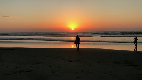 Silhouette-Einer-Jungen-Frau,-Die-Allein-Am-Strand-Steht-Und-Die-Sonne-Direkt-über-Dem-Horizont-Des-Ozeans-Untergeht