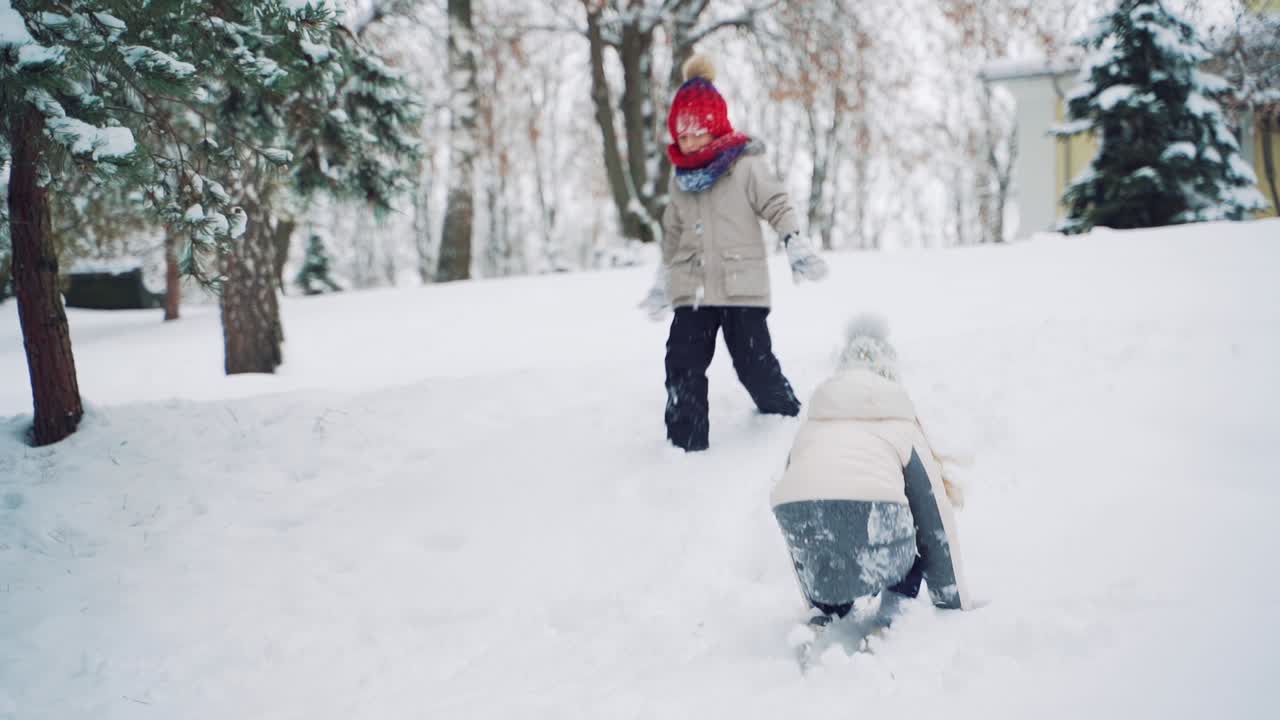 Cheerful children are running through the snow and playing together in the park in the winter around trees. Slow motion