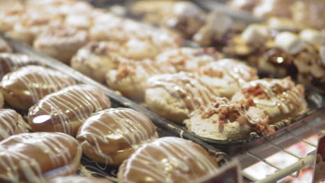 slow panning shot left to right of donut shop display case with large variety of sweets and flavors in warm light