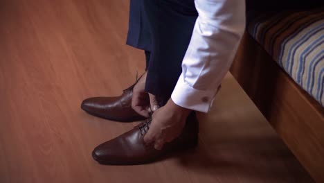 a man finishing dressing himself in a formal attire, fastening his shoes