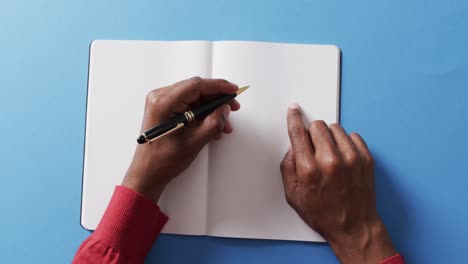 close up of hand writing with pen on book with copy space on blue background in slow motion