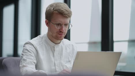 calm european man is working with laptop in office or modern coworking space, portrait of handsome guy