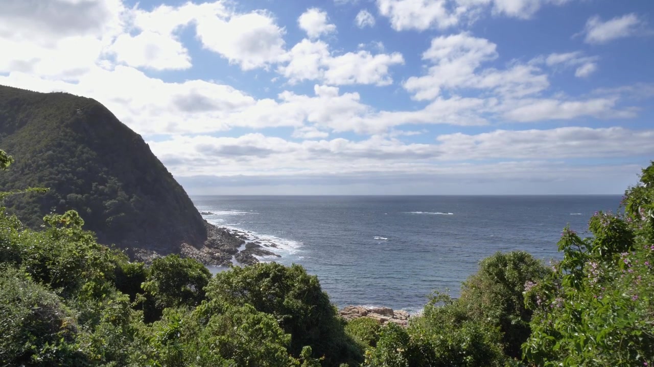 Una vista mozzafiato di una costa frastagliata dove una montagna verdeggiante incontra l'oceano blu profondo, con onde che si infrangono dolcemente contro le coste rocciose alla foce del fiume Storm nel Parco Nazionale Tsitsikamma.