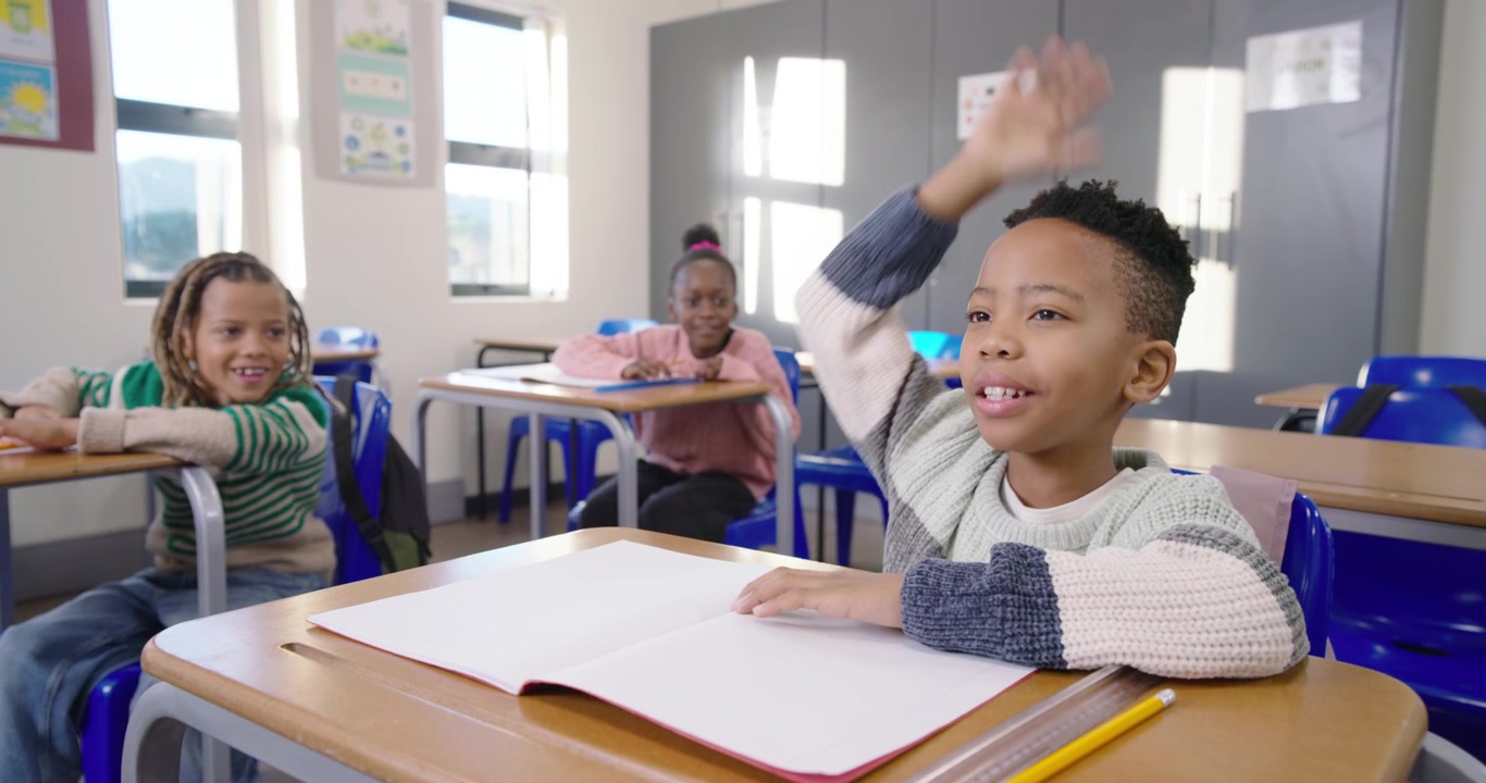 African American classmates watching boy answering teacher question at front desk, tapping notebook