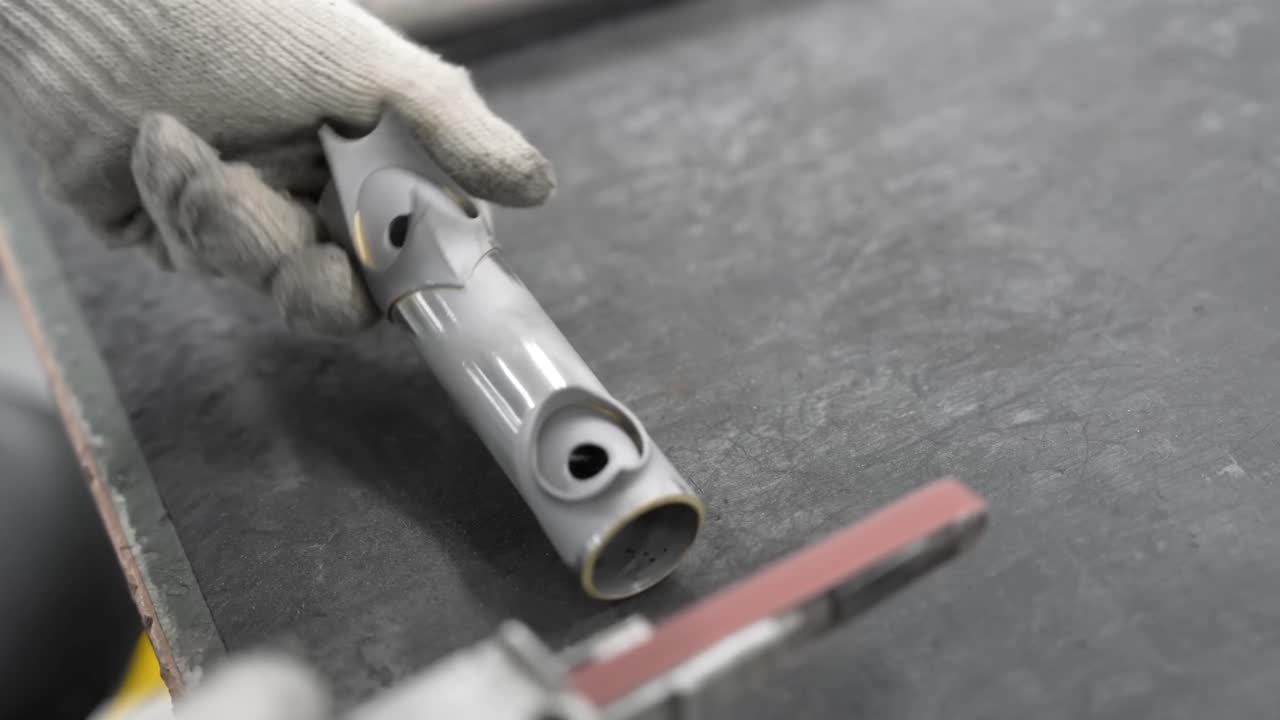 Close up of gloved hands using a small belt sander to smooth the surface of a metal bicycle frame component