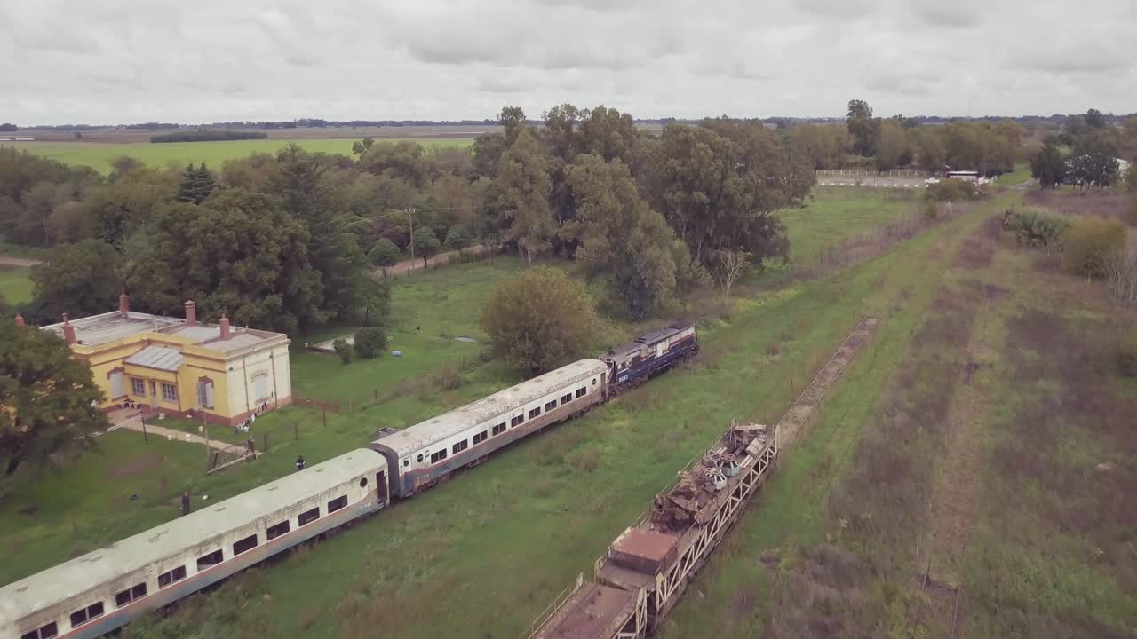 aerial view of an old train in motion with a rural school background and abandoned trains in,Buenos Aires