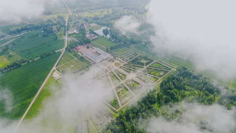 elegant aerial of historic french-style palace gardens glowing through clouds