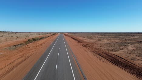 endless bitumen through the outbacka drone’s-eye view of a lone sealed road cutting through australia’s vast, rugged outback—endless skies, red earth, and total isolation