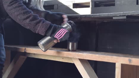 woman pouring a flask of hot coffee in nature hide