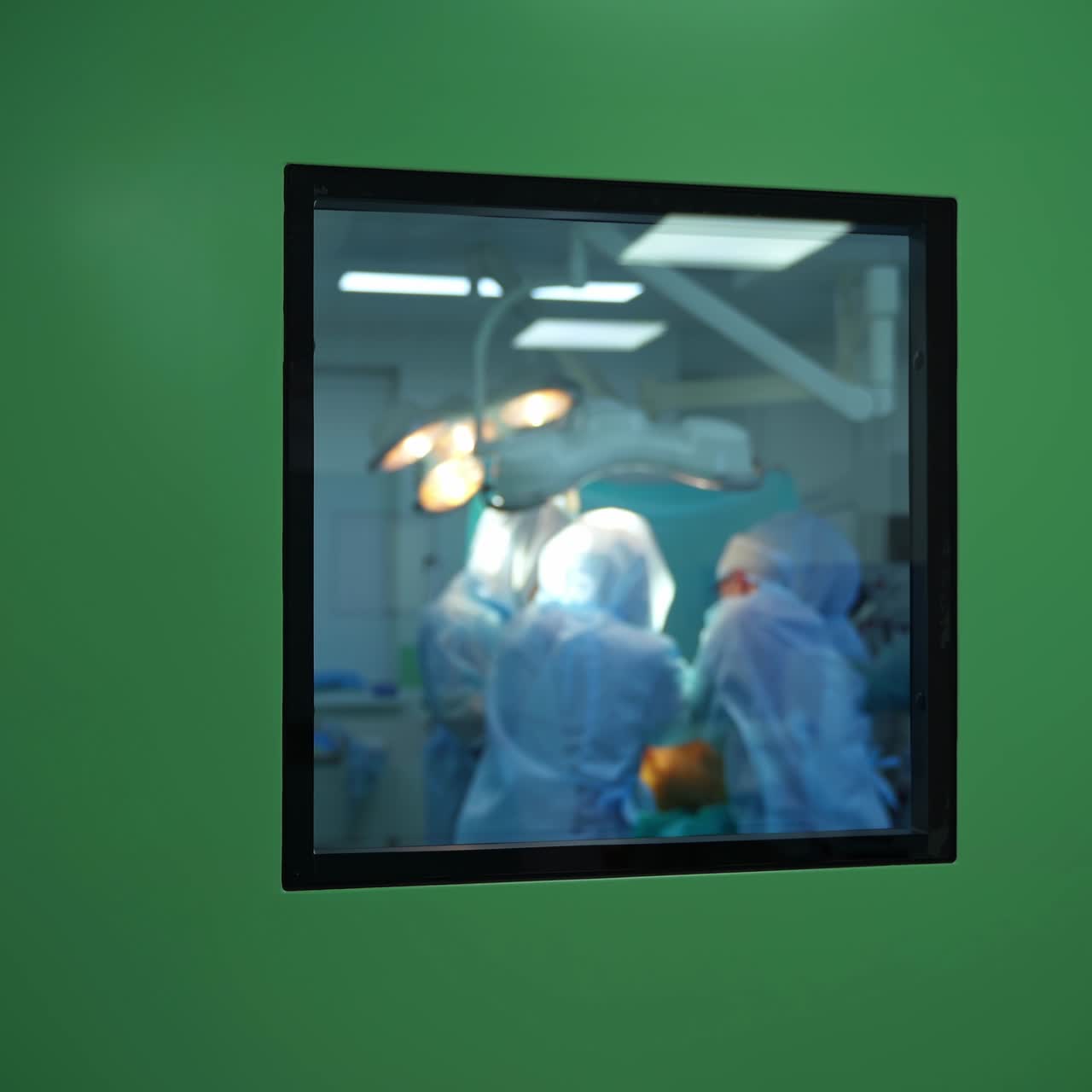 Surgery in the operating room. Teamwork of doctors in blue uniform doing an operation. View through the window from the corridor.