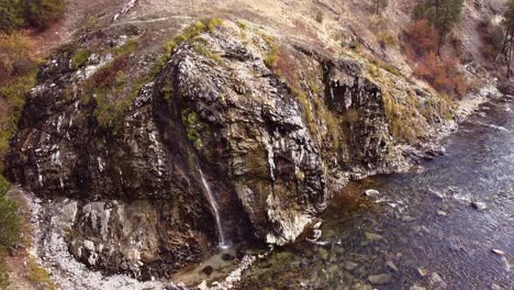 aerial drone shot approaching a hot spring waterfall panning down rising above in boise national forest in idaho with the spring flowing into a pool below beside boise river