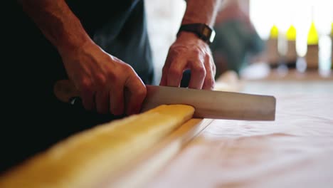 toma panorámica en cámara lenta de un chef italiano cortando pasta hecha a mano sobre una mesa de corte de madera cruda