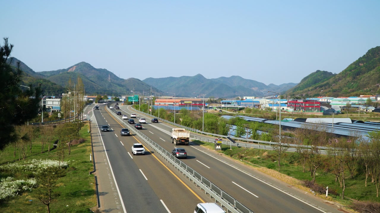 柔らかな朝日の下、肥沃な丘と段々畑の横を車が走る高速道路。韓国錦山郡。