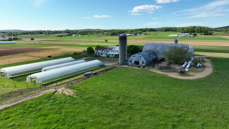 aerial establishing shot of american farm in countryside with greenhouse and stable during sunny day usa, drone orbit