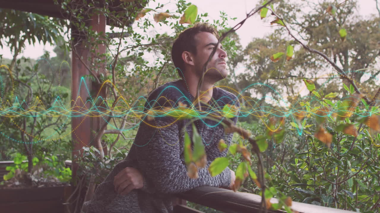 Designer leaning on porch railing, analyzing waveform overlay amid leaves showcasing technology