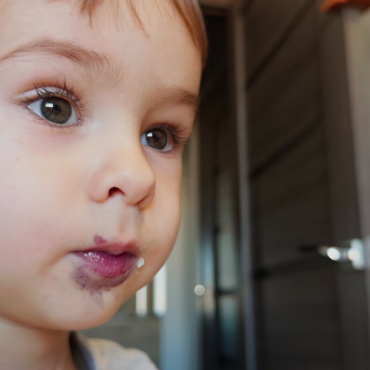 Bellissimo neonato caucasico con una macchia viola intorno alla bocca. Primo piano. Adorabile bambino che mangia un mirtillo
