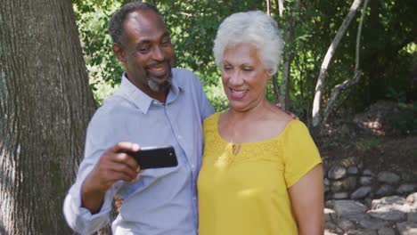 senior african american husband and mixed race wife laughing and taking photo in the garden