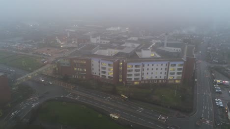 Misty-foggy-hospital-UK-NHS-building-town-traffic-aerial-high-angle-orbit-right