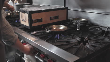 igniting an industrial stove in a commercial kitchen to cook steak in a pan, medium shot in slow motion