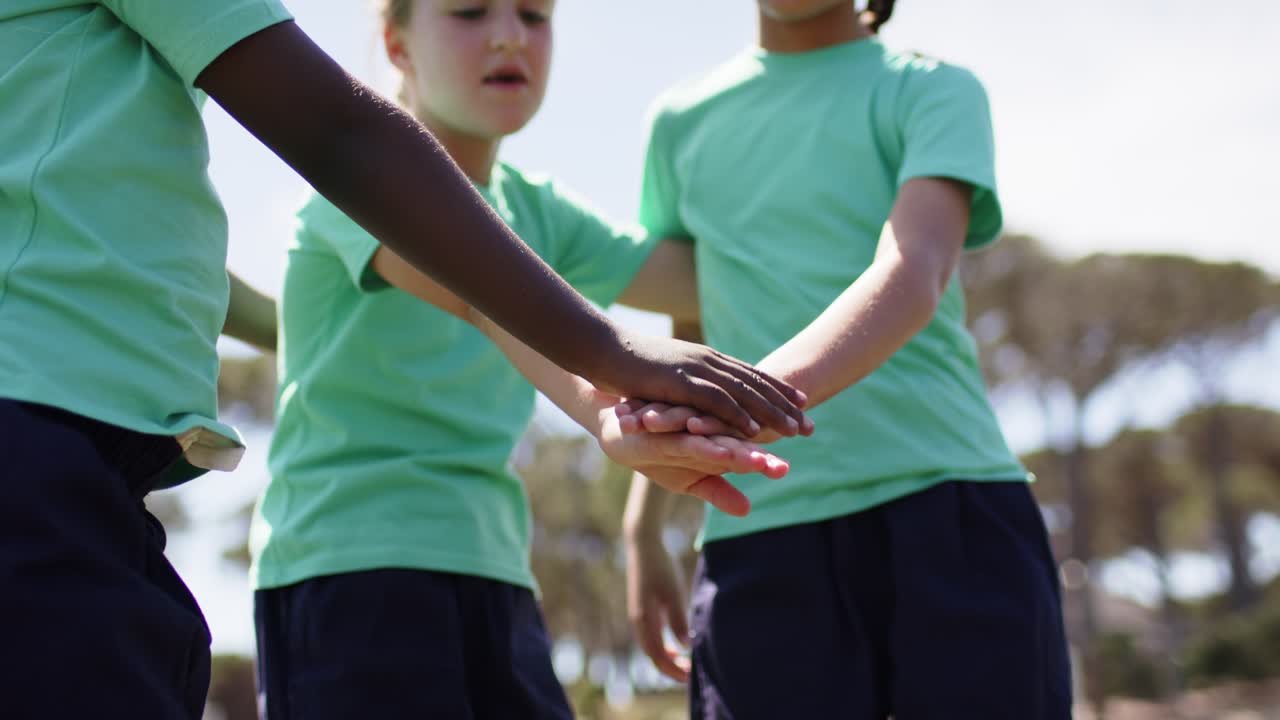 Diverse teenage females huddling in mint-green tees, stacking hands, raising arms on field pre-game