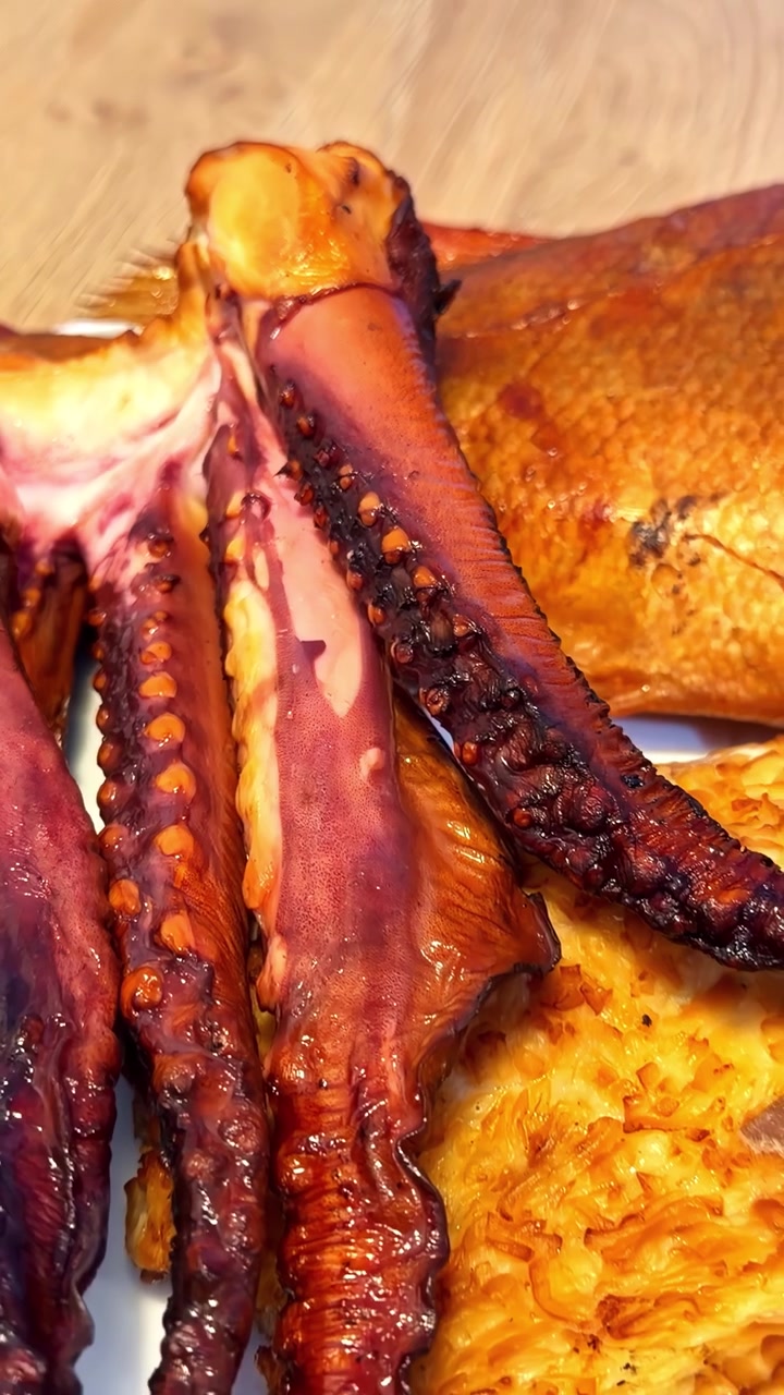 Vista dettagliata di tentacoli di polpo affumicati disposti su una superficie di legno. Adatto per presentazioni culinarie o marketing di prodotti ittici