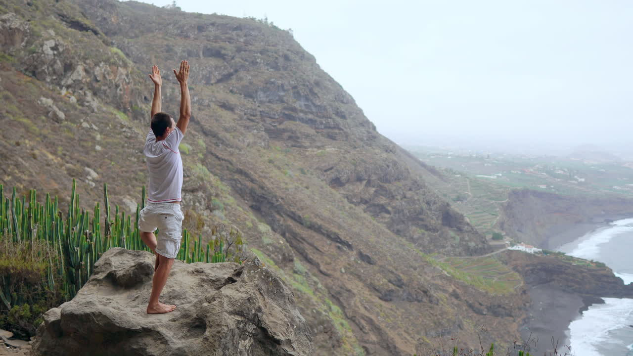 contra el pintoresco panorama de las montañas y el océano, un joven en forma armoniza la meditación y el ejercicio a través del yoga de saludo al sol
