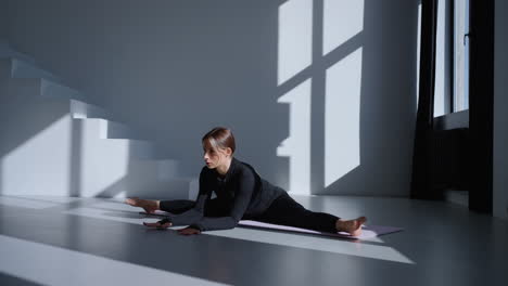 woman doing a yoga split stretch on a mat in a studio