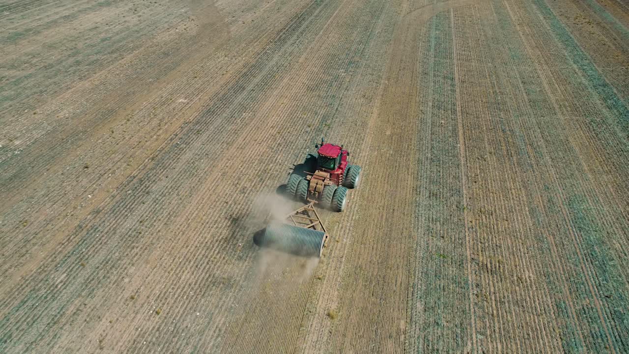 Aerial video of a red tractor towing a stone roller through a bare paddock