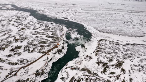 Aerial-high-angle-shot-showing-Godafoss-Waterfall-and-snowy-icelandic-landscape-during-winter---Snow-covered-hills-and-cold-river