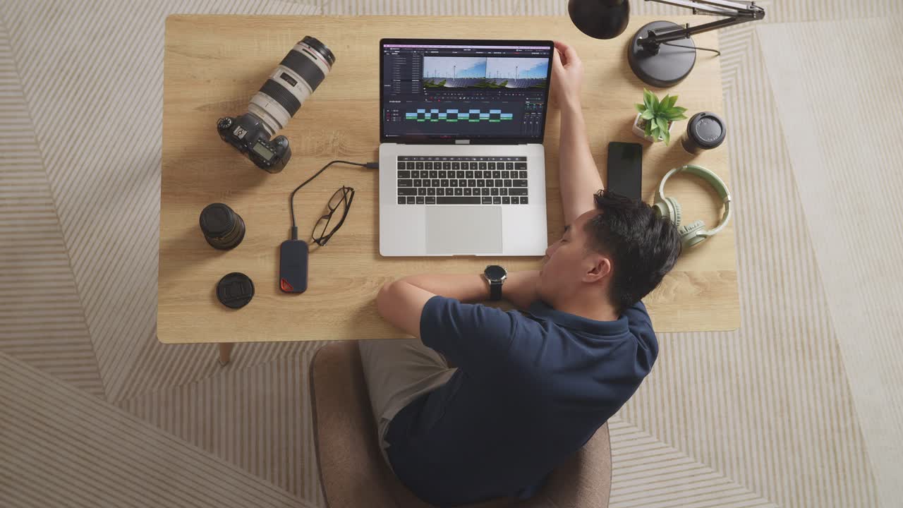 Top View Of Asian Male Editor Sleeping While Sitting In The Workspace Using A Laptop Next To The Camera Editing The Video At Home