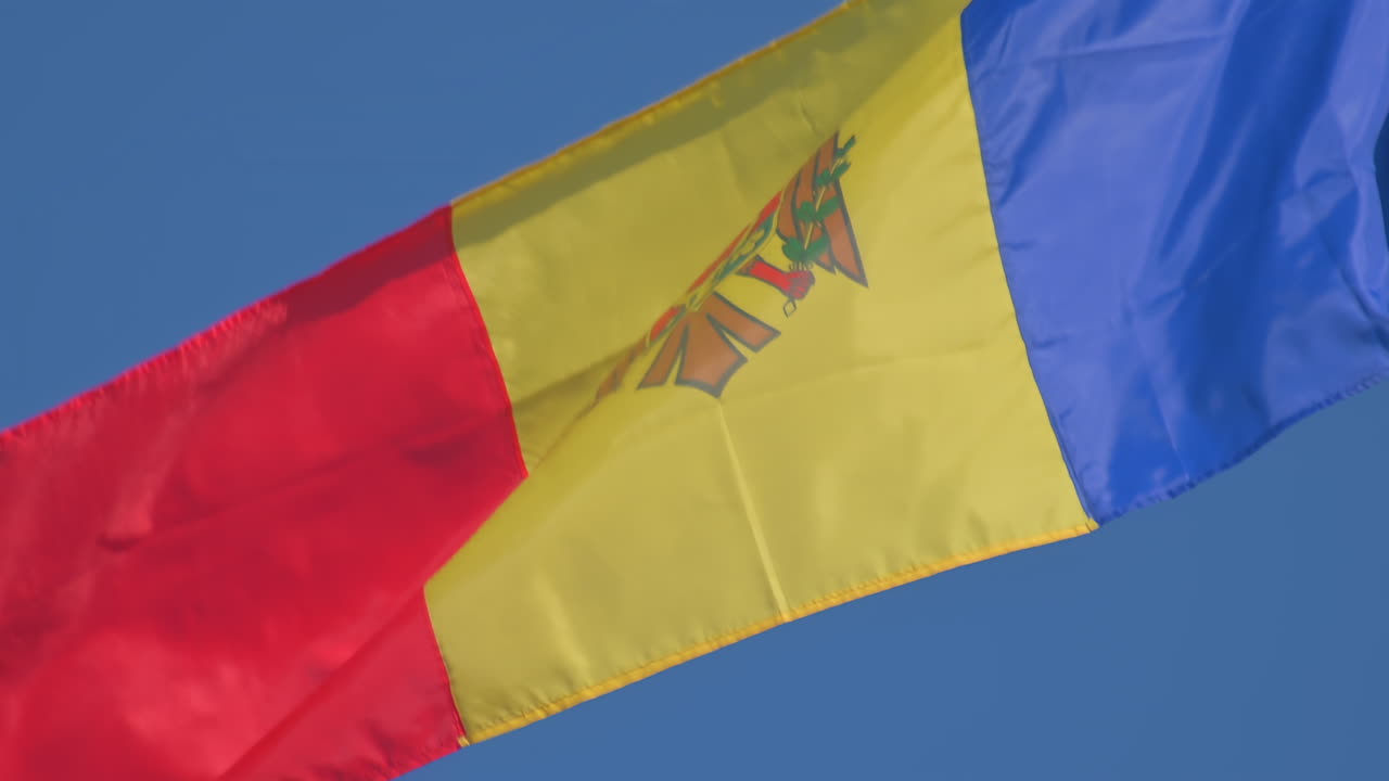 A vibrant Moldovan flag flutters in the wind against a bright blue sky. The colors of red, yellow, and blue symbolically represent the nation's heritage and pride