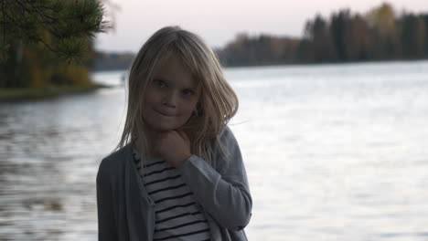 portrait of beautiful scandinavian little blonde caucasian shy girl with lake in background