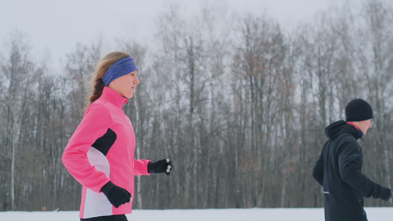 젊은 남자와 여자는 아침에 겨울 숲에서 뛰었습니다. 헐렁한 재킷을 입은 여자 검은 재킷을 입은 남자가 겨울 공원을 달리고 있습니다. 건강한 생활 방식 행복한 가족.
