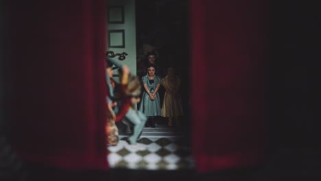 a group family of small glass porcelain doll figures figurines inside a dark moody hand painted antique vintage red curtain house in shadow miniature