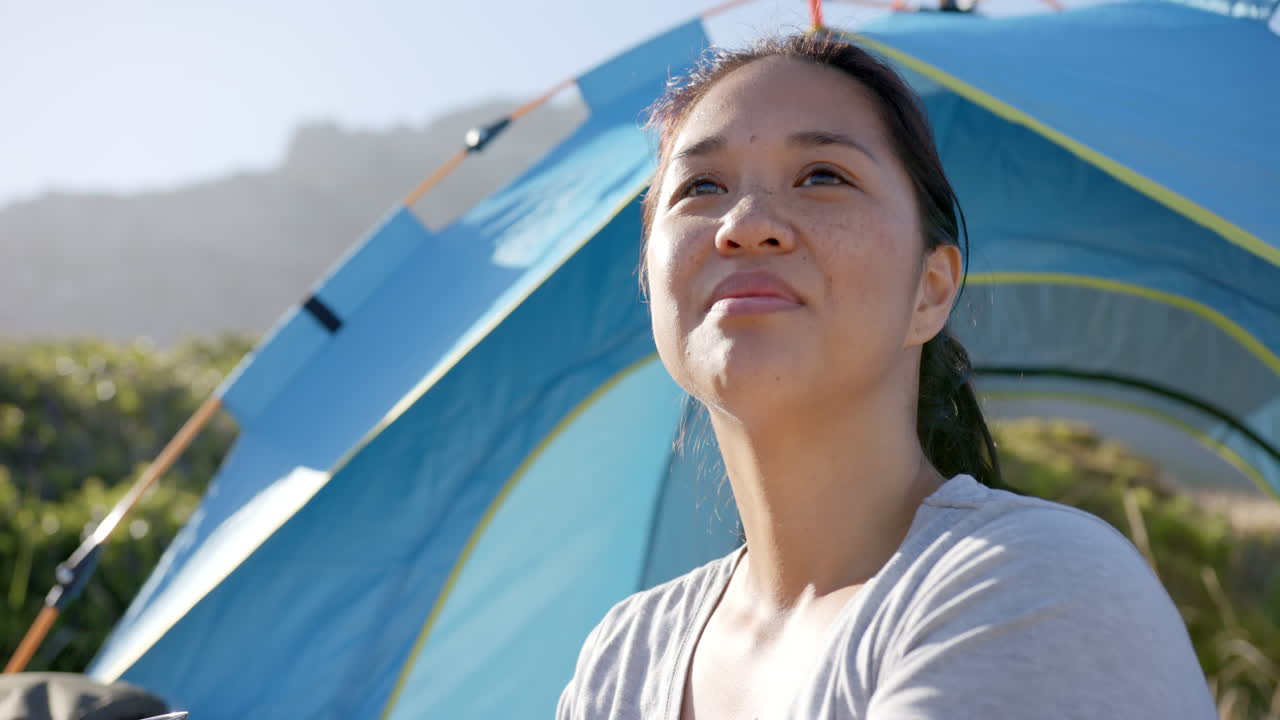 Smiling woman enjoying outdoor camping in front of blue tent during mountain hike