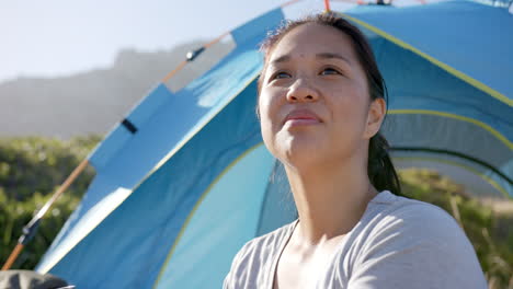 smiling woman enjoying outdoor camping in front of blue tent during mountain hike