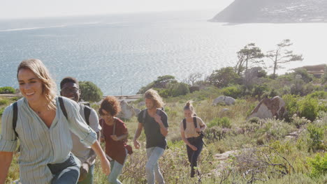 group of young friends hiking up cliffs on coastal path through countryside together