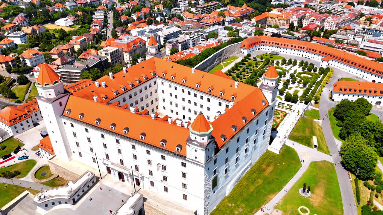 Flight over the orange roof of the Bratislava Castle. Beautiful green gardens and flower-beds around