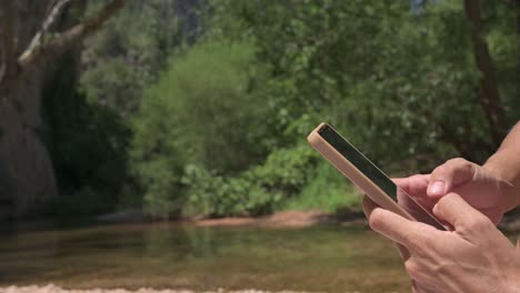 young woman checking her smartphone while seated by a calm river in summer