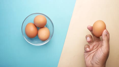 person holding an egg with a bowl of eggs on a table