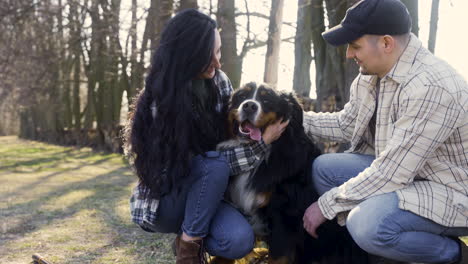 close-up view of caucasian couple squatitng and petting their dog in the countryside