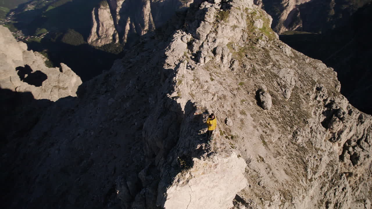 hombre en una cornisa rocosa precaria con vistas al pintoresco valle, alpes