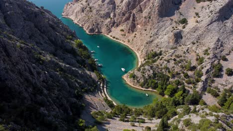 Majestic-turquoise-bay-of-Zavratnica-in-Mediterranean-Croatia,-aerial-tilt-down-of-boats-and-swimmers