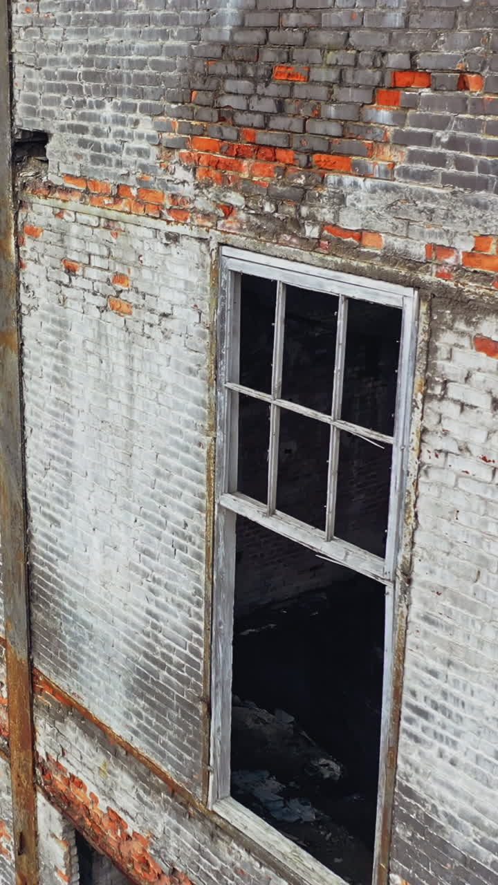 Damaged brick building without windows after the war. Close view of a destructed house with many holes in the wall. Camera moves top down Vertical video