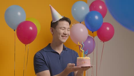 retrato de estudio de un hombre con un sombrero de fiesta celebrando su cumpleaños soplando velas en el pastel
