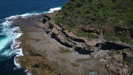 waves splashing on the rocky shore of wybung head lookout in frazer park, new south wales, australia - drone shot