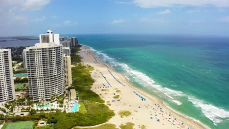 Aerial-drone-shot-very-slowly-rising-above-the-beach-looking-towards-the-buildings-including-the-Ritz-Carlton-residences,-the-beach,-and-the-Atlantic-ocean-on-a-sunny-day-with-blue-skies